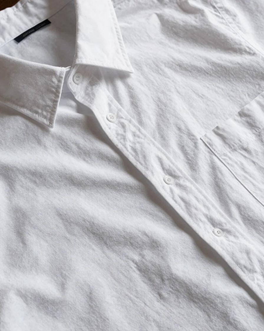 Gros plan sur le tissu d'une chemise en coton blanc, plis naturels et texture visible, lumière douce et naturelle, cadra